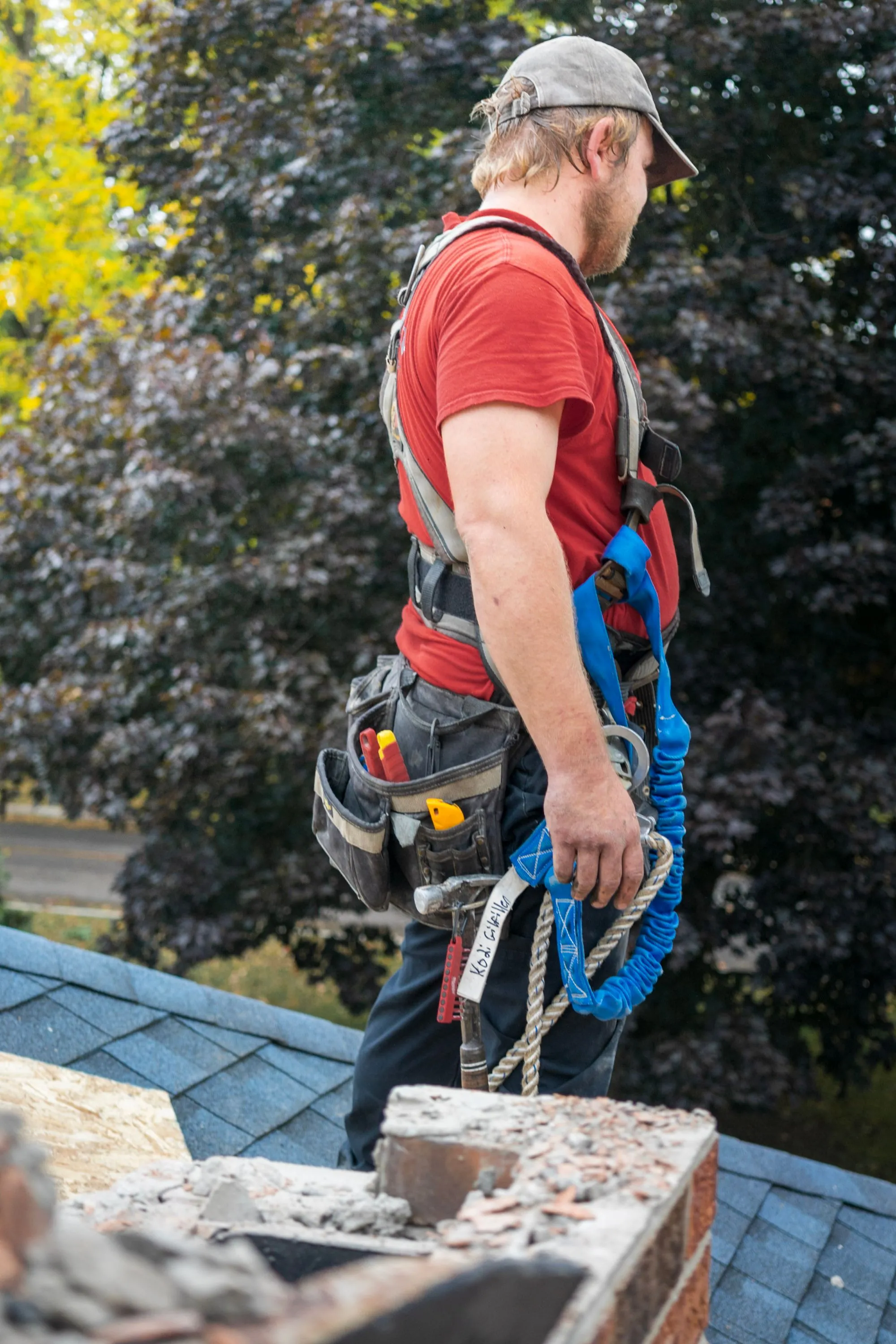A roofer standing beside a chimney on a residential roof during a survey