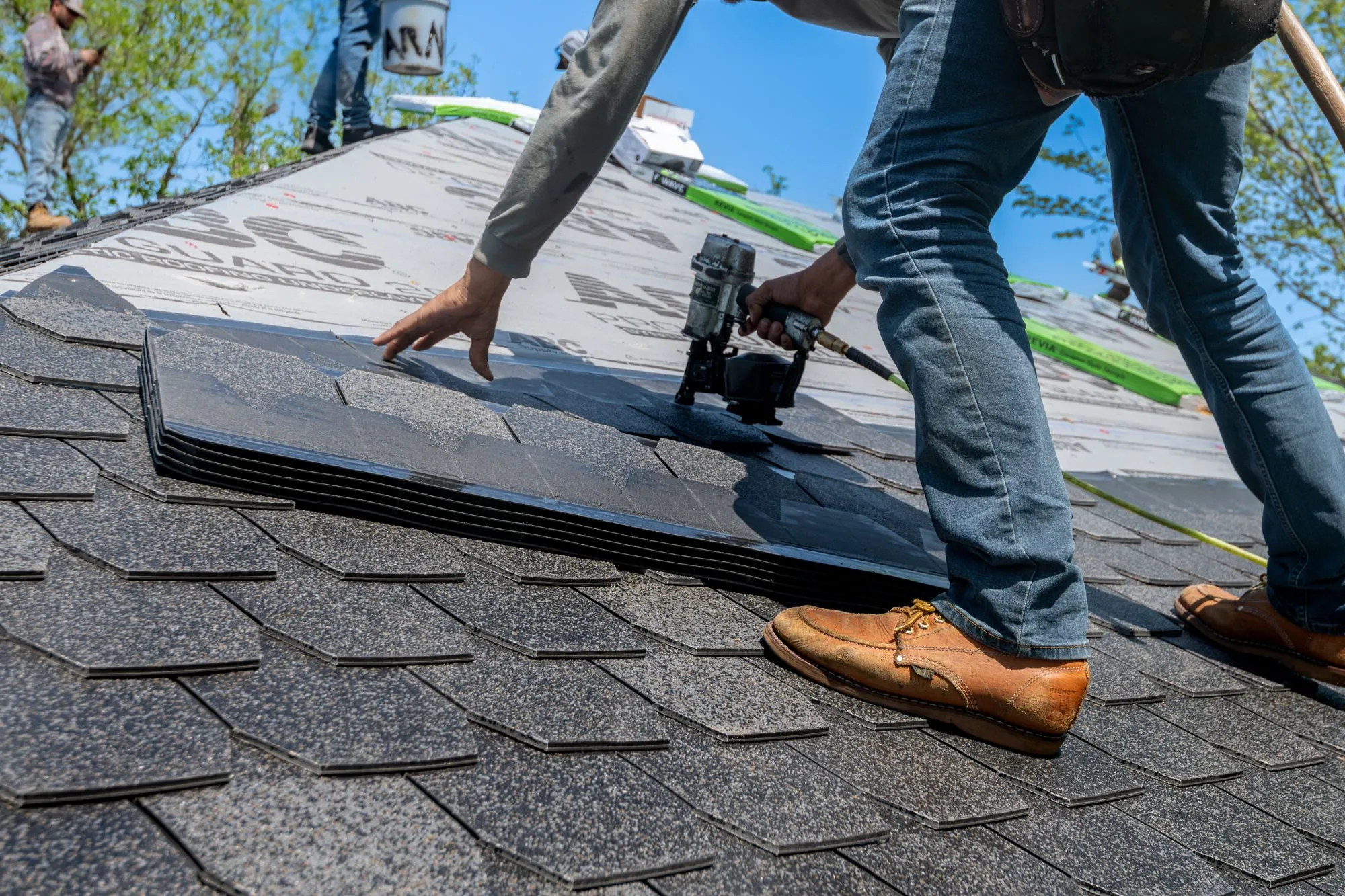 A roofer setting a replacement shingle and driving it home with a nail gun