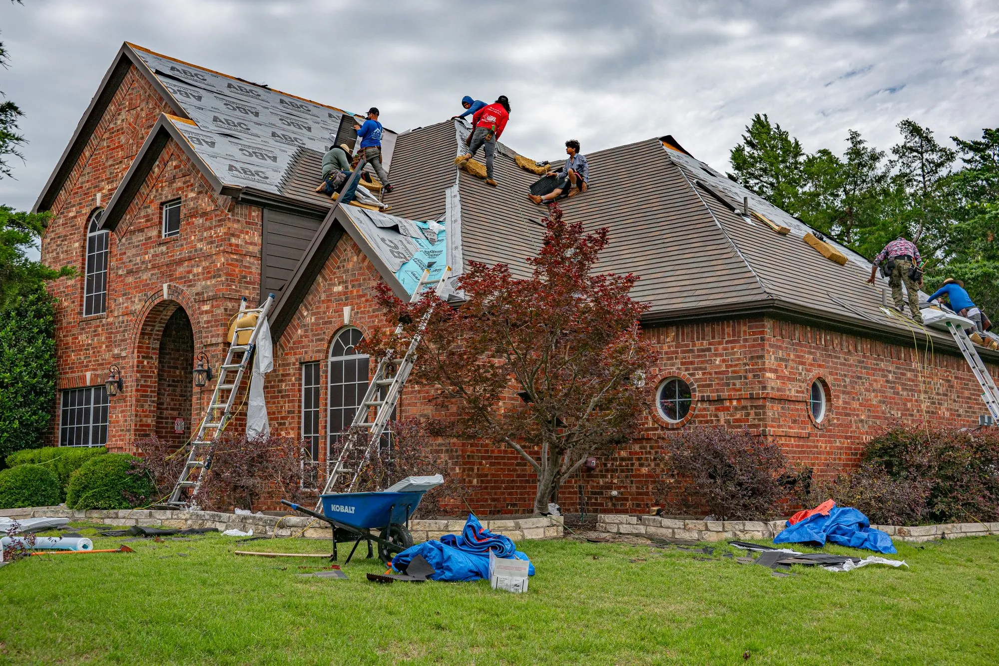 A crew working across the slopes of a brick house after storm damage