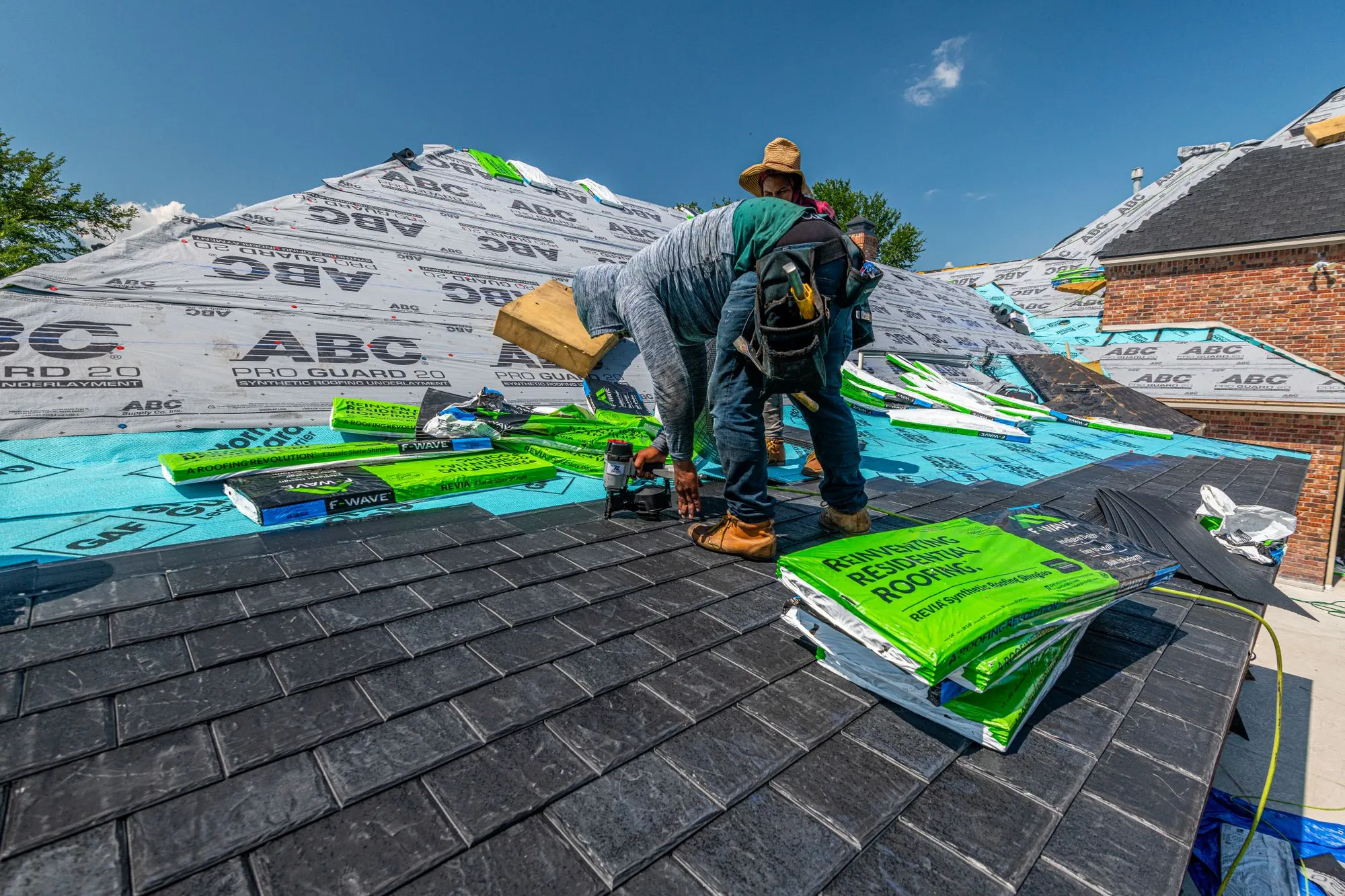 A roofing crew moving bundles of shingles across a freshly underlaid roof