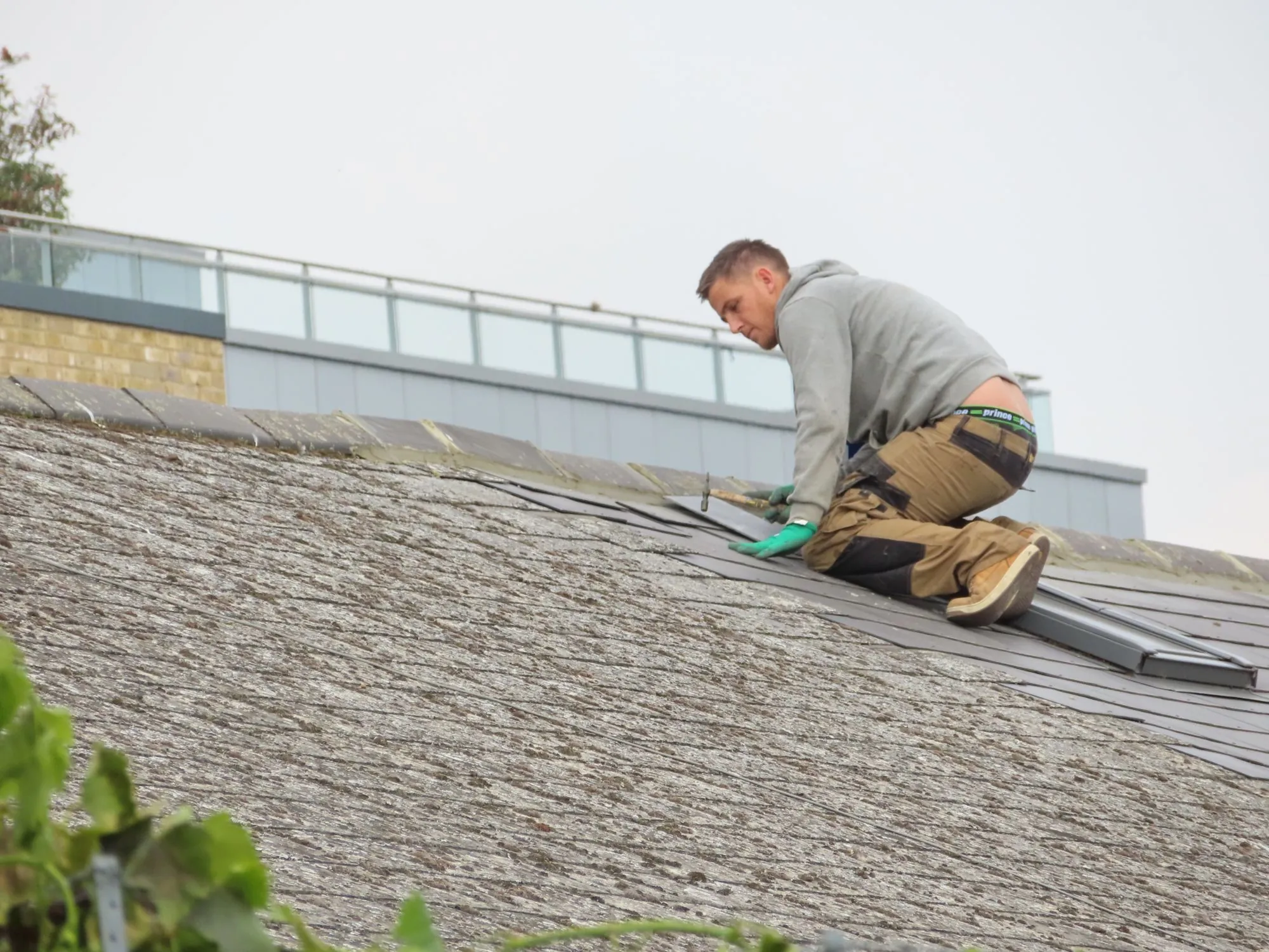 A roofer kneeling to work a long run of roof covering