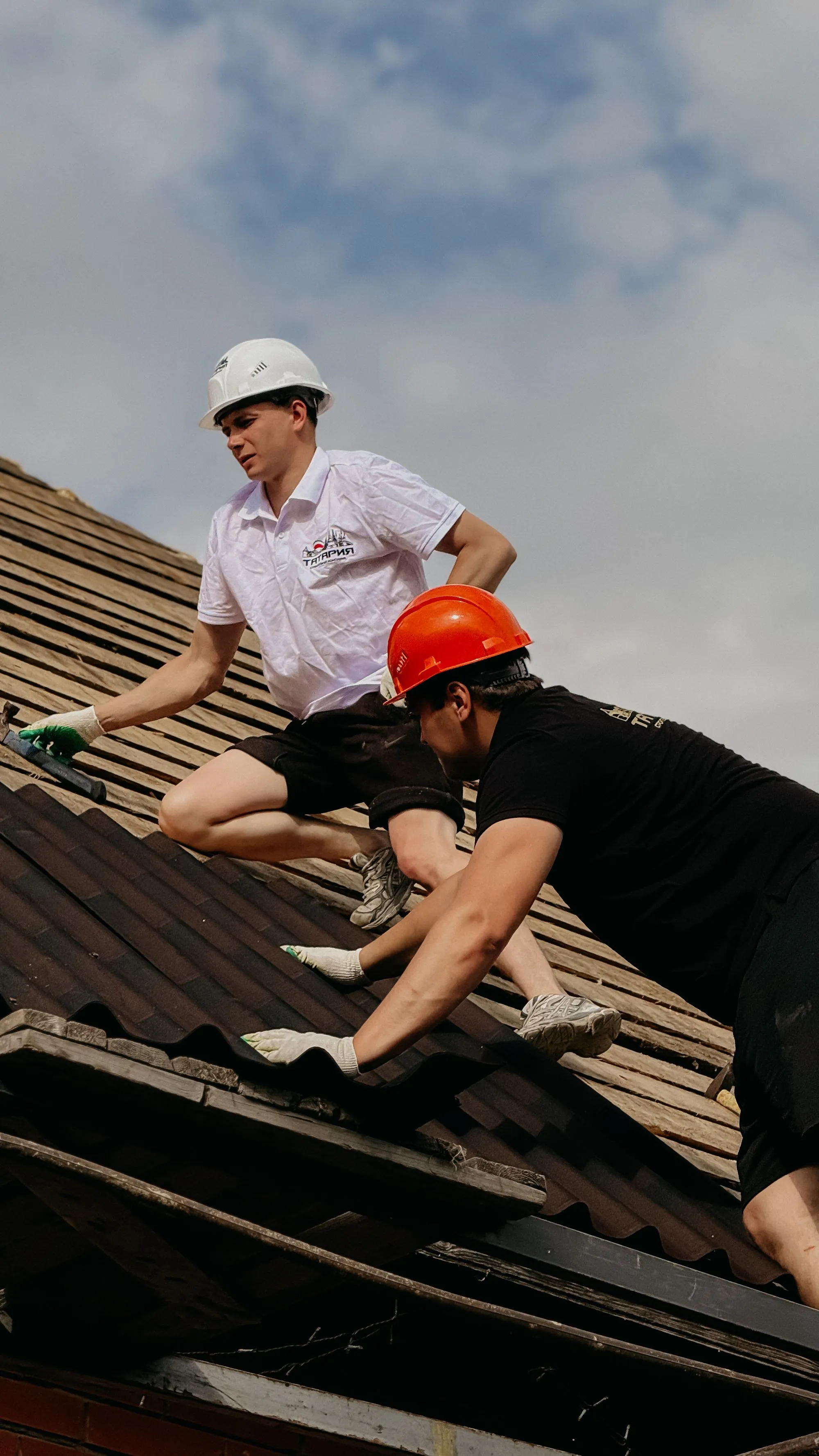 Two roofers in hard hats working a roof slope together