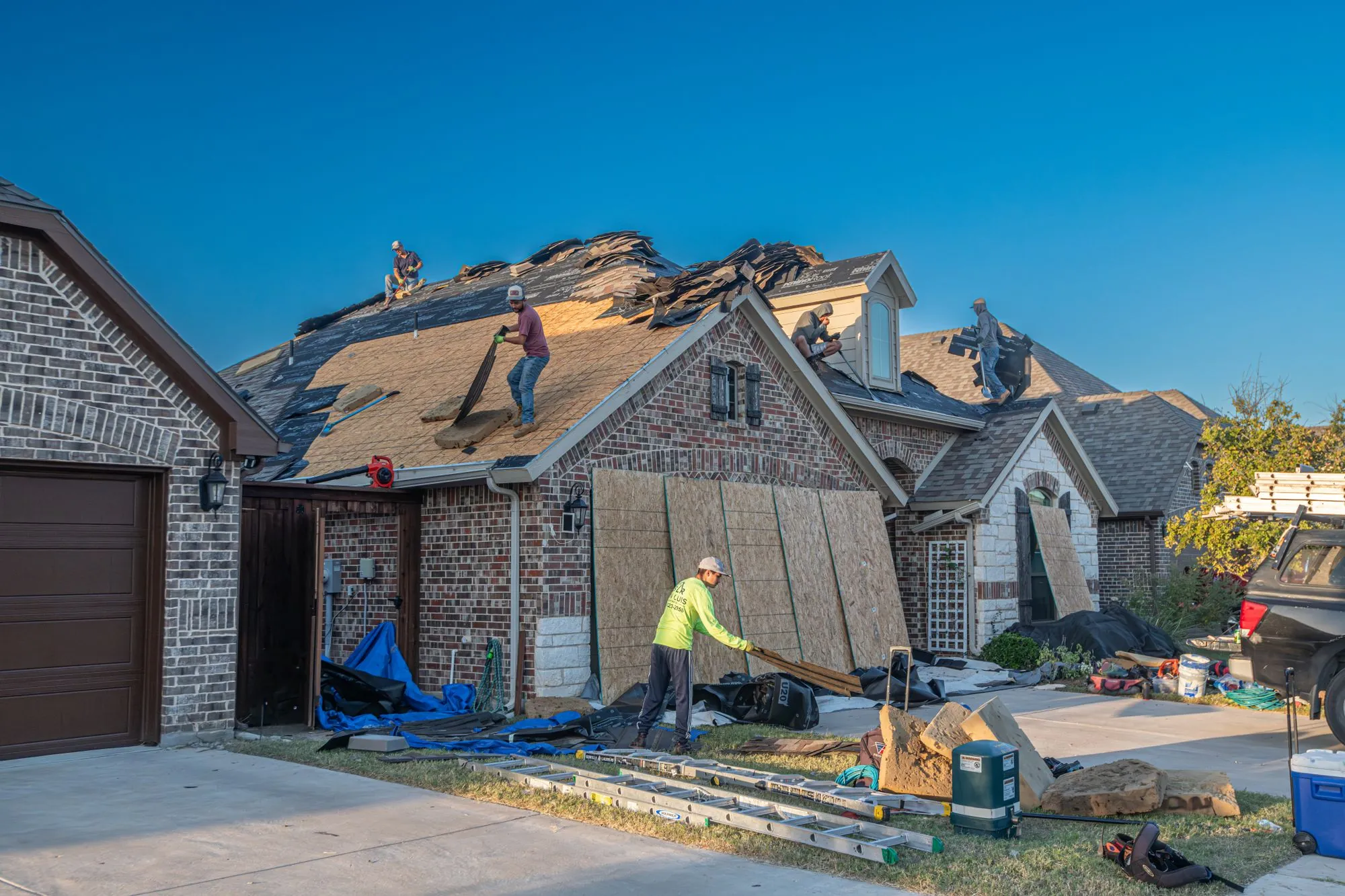 A roofing crew at work across the slopes of a large brick house