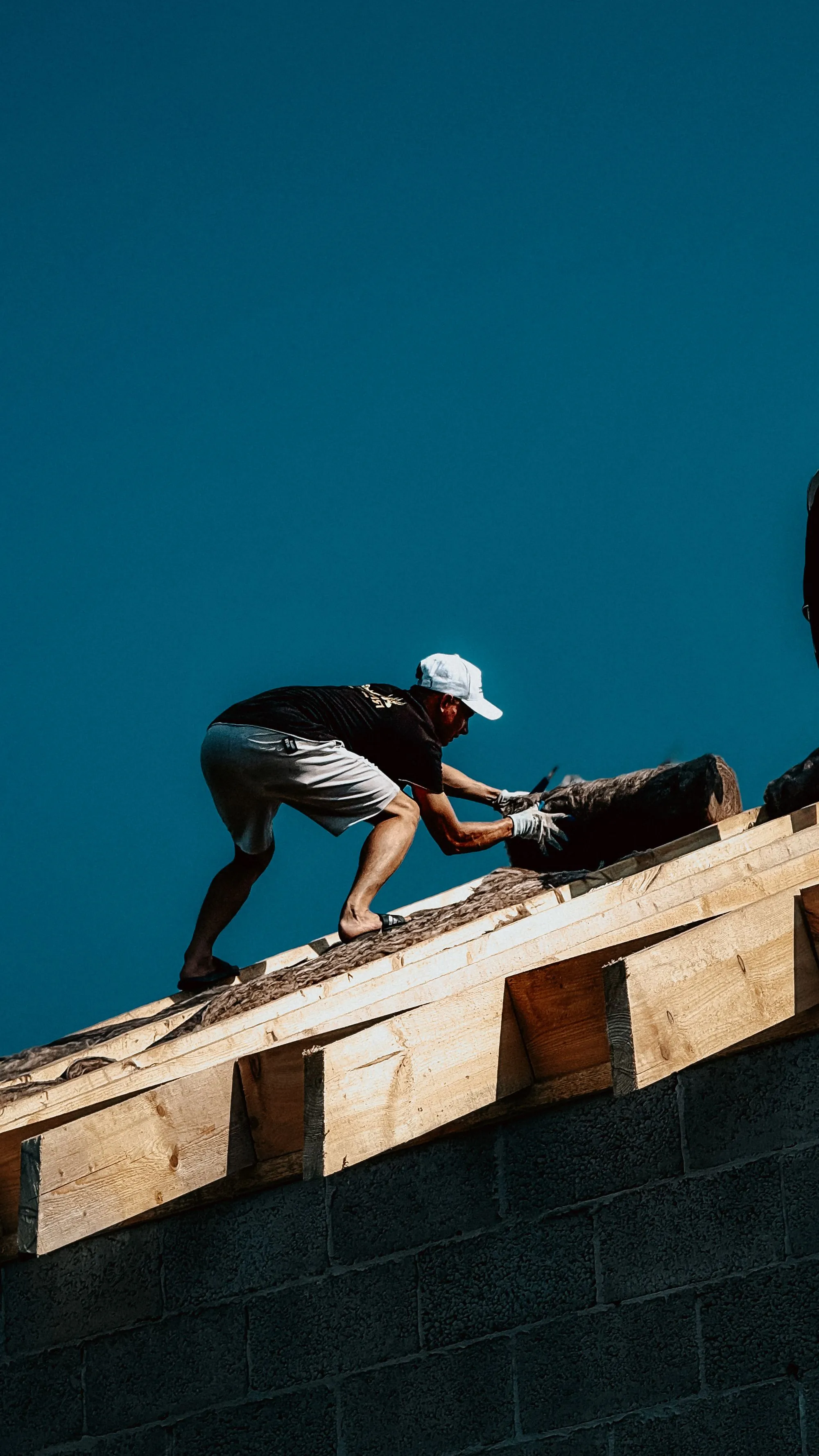 A roofer working along a bare roof ridge against a deep blue sky