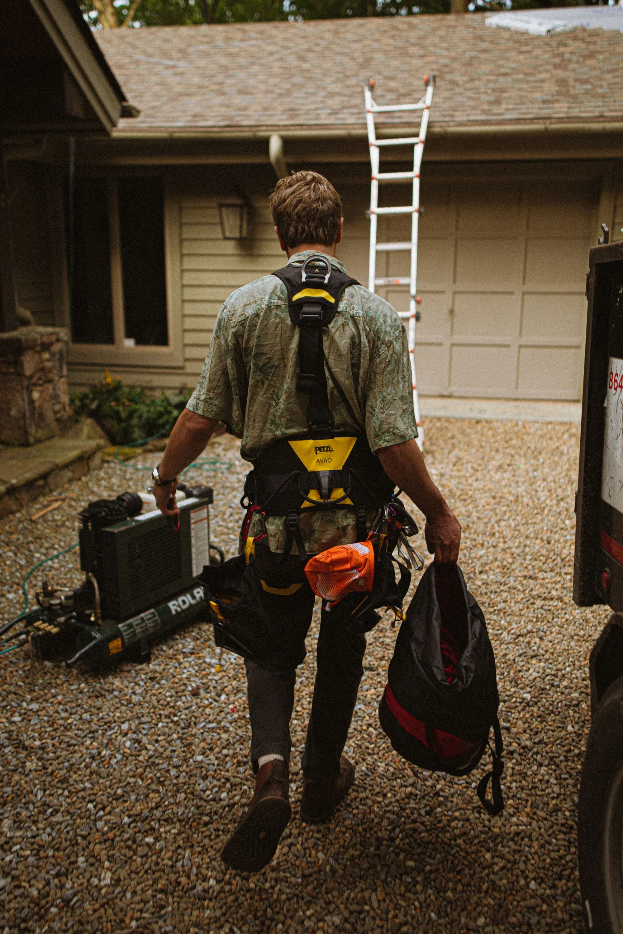 A roofer carrying tool bags away from a house with a ladder still set against it
