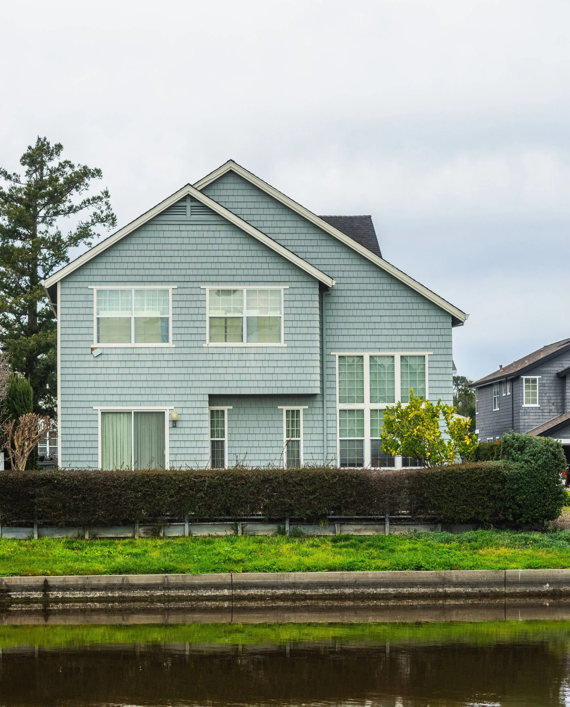 A detached suburban house with a shingled roof beside still water